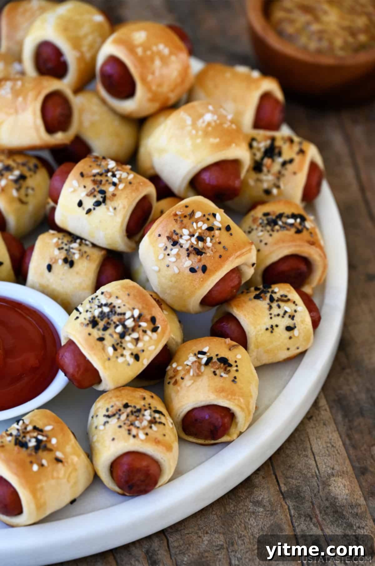 Pigs in a blanket piled on a serving platter with a small bowl containing ketchup.
