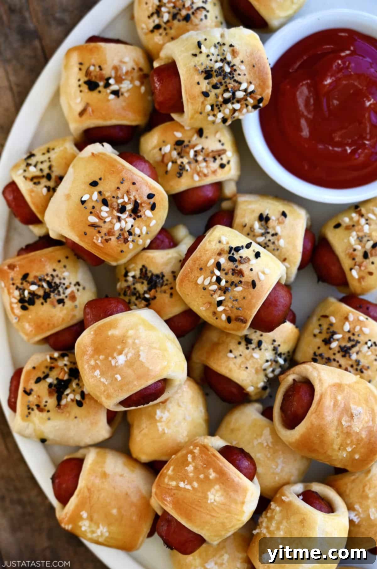 Classic pigs in a blanket piled on a plate with a small bowl containing ketchup for dipping.