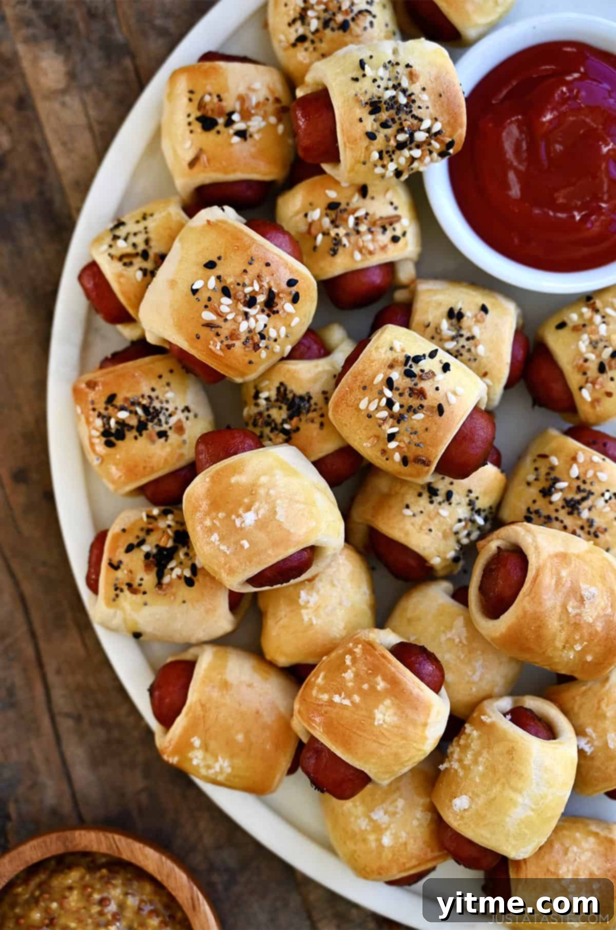 Mini cocktail sausages wrapped in Pillsbury crescent roll dough and garnished with everything bagel seasoning on a serving plate.