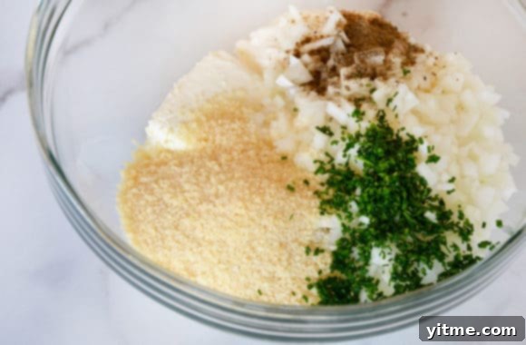 A glass bowl containing ingredients for making a creamy, cheesy dip before mixing