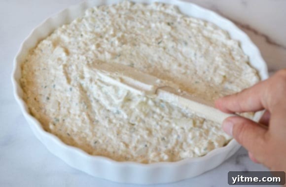 A white baking dish with Warm and Cheesy Onion Dip and a spatula, ready to be served