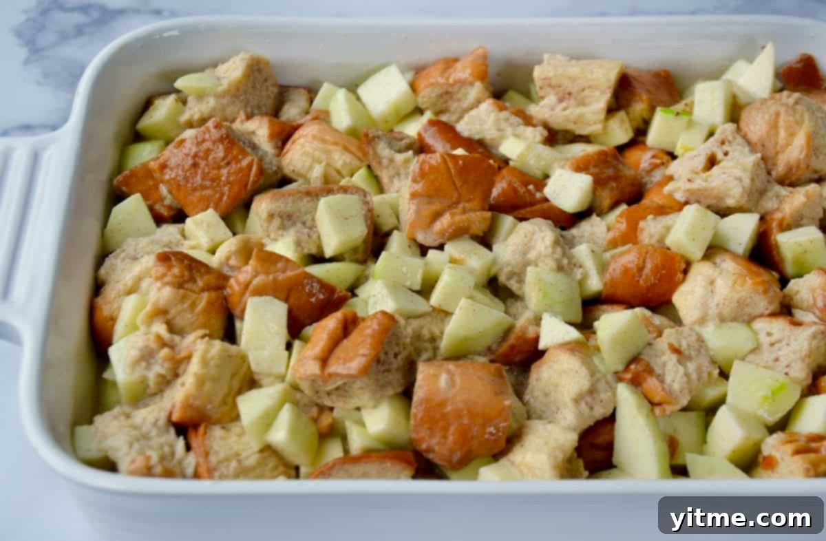 Cubes of brioche bread, chopped apples and a vanilla custard in a baking dish before going into the oven to bake.