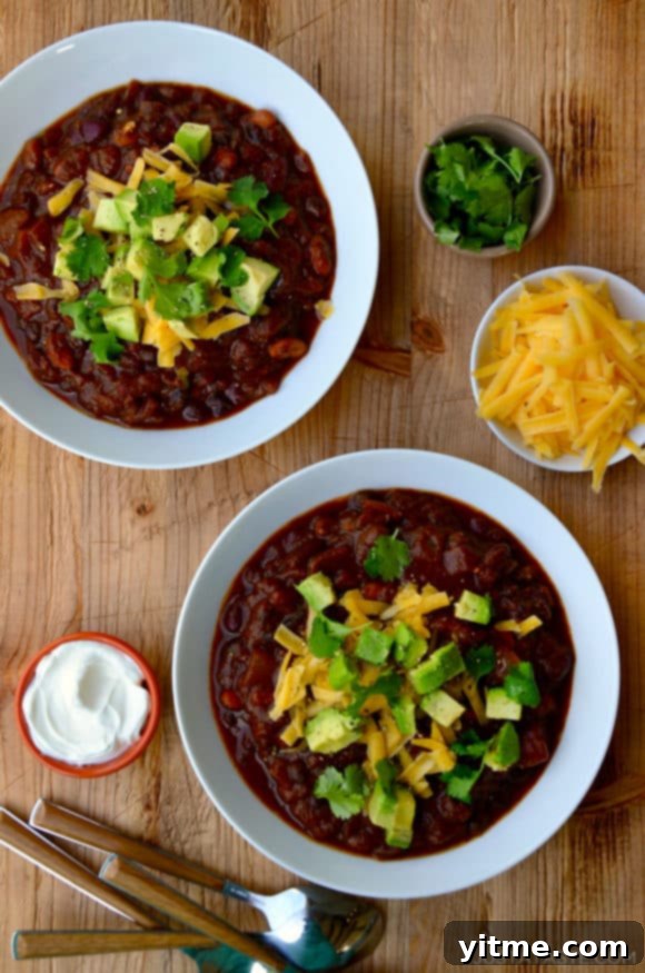 Two white bowls filled with chili and smaller bowls surrounding them containing chili toppings