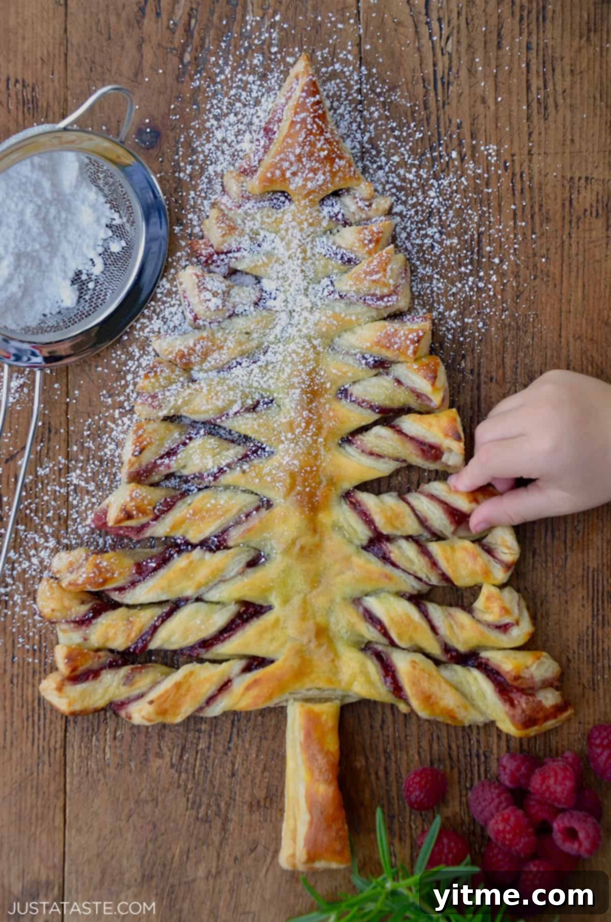 Child's hand reaching for a Christmas Tree Puff Pastry sprinkled with confectioners' sugar.