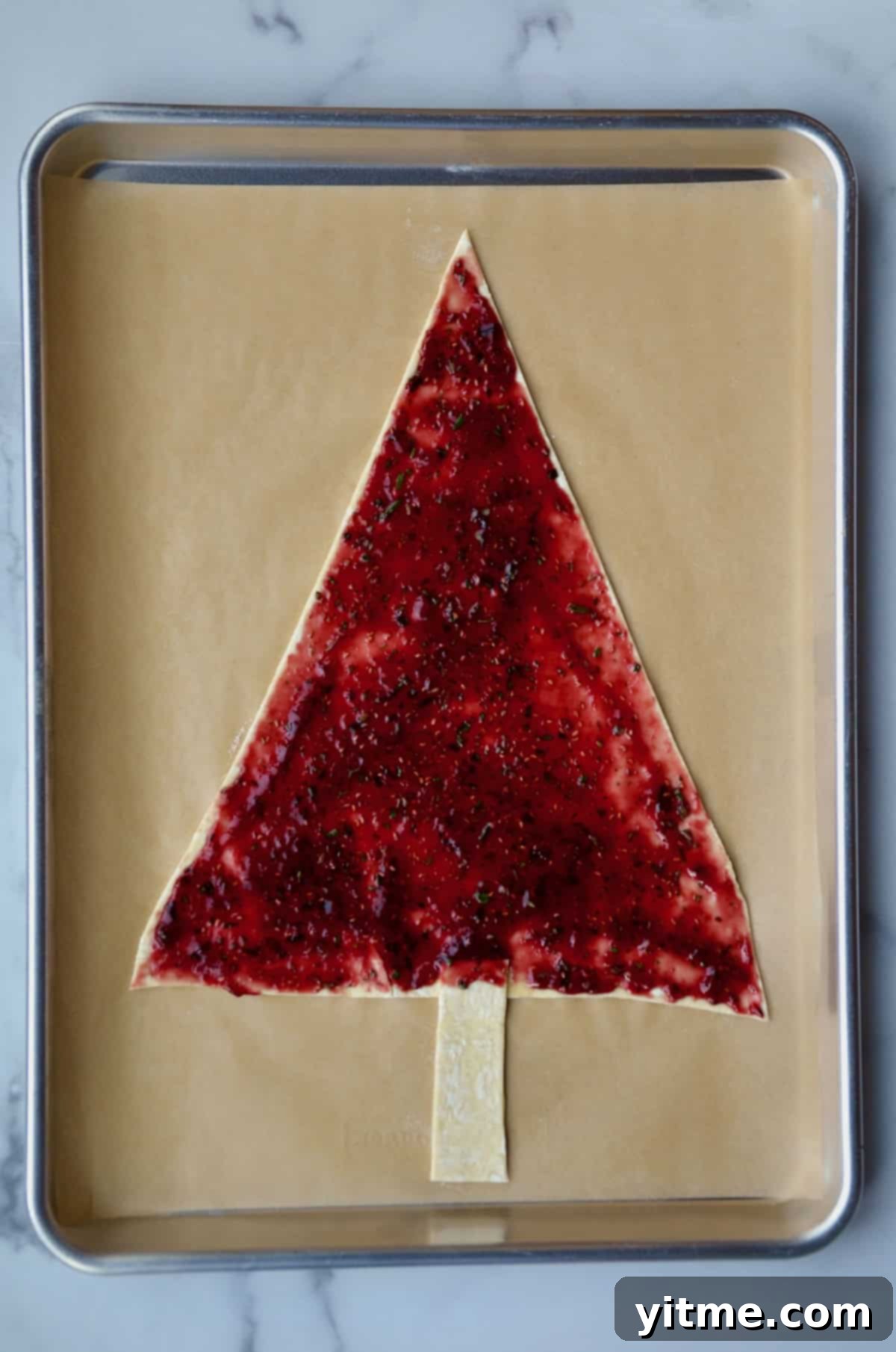 Jam spread over tree-shaped puff pastry on parchment paper lined baking sheet.