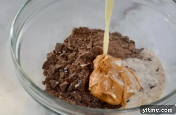 Heavy cream being poured into bowl containing chopped chocolate and creamy peanut butter