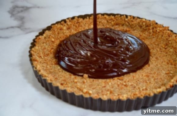 Chocolate mixture being poured into pretzel tart shell