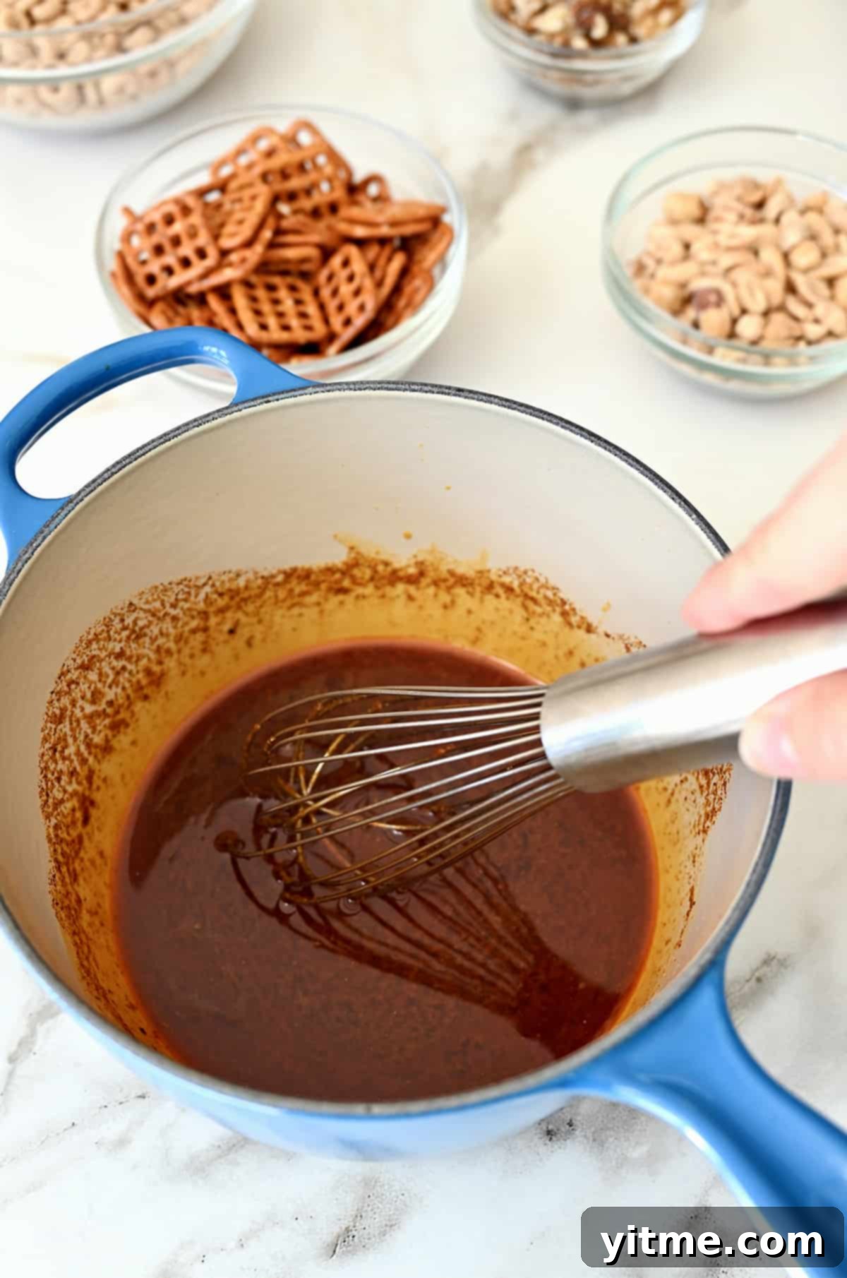 A hand holding a whisk mixes a seasoned sauce in a small saucepan.