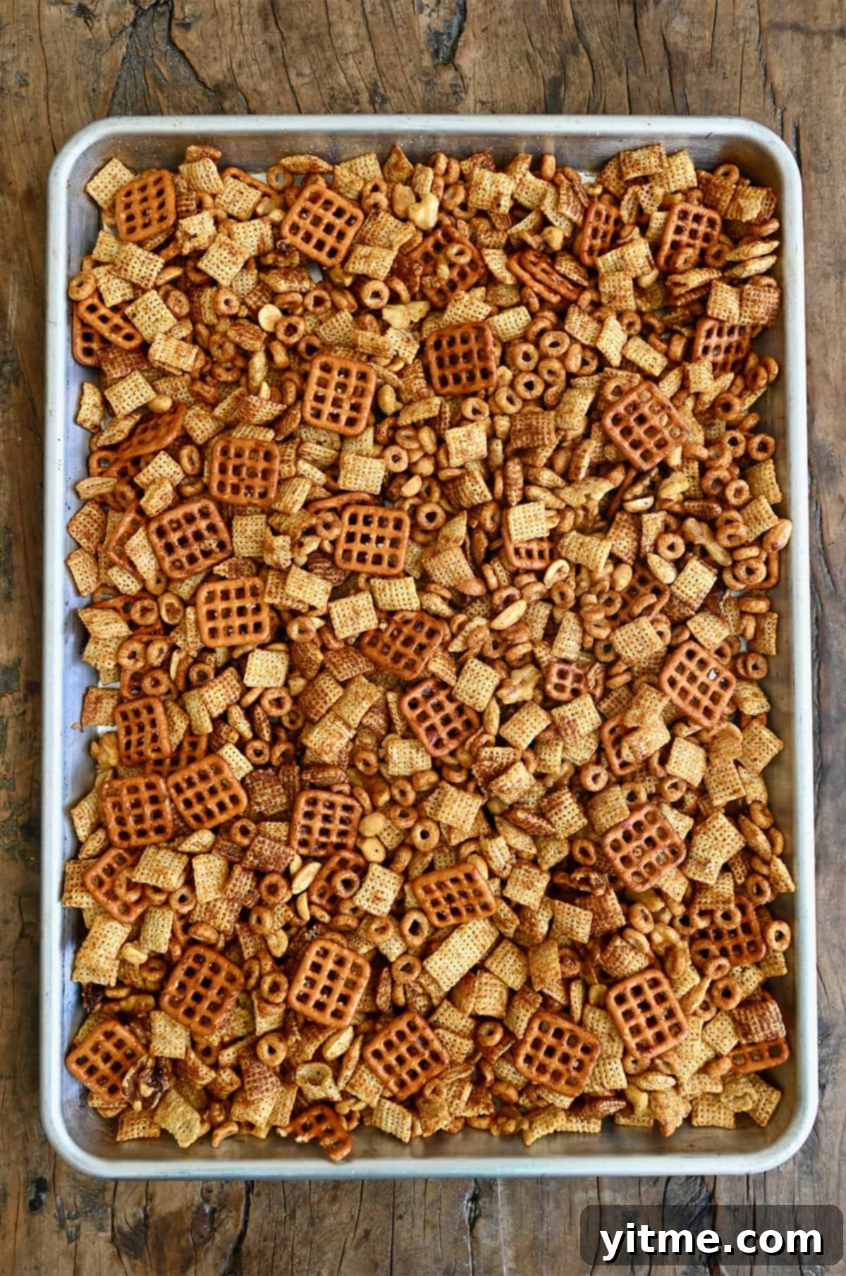Chex party mix with Cheerios, nuts and pretzels, cooling on a baking sheet.