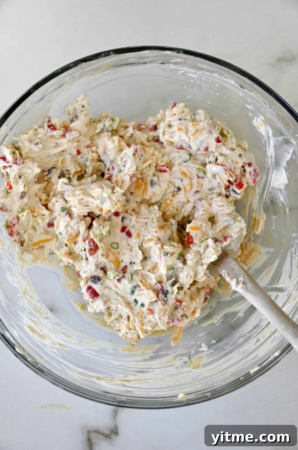 Cheddar, cream cheese, and bacon mixture in a glass bowl.