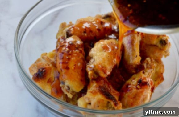 Chicken wings in a glass bowl being coated with a glossy, reddish-brown sesame sauce.