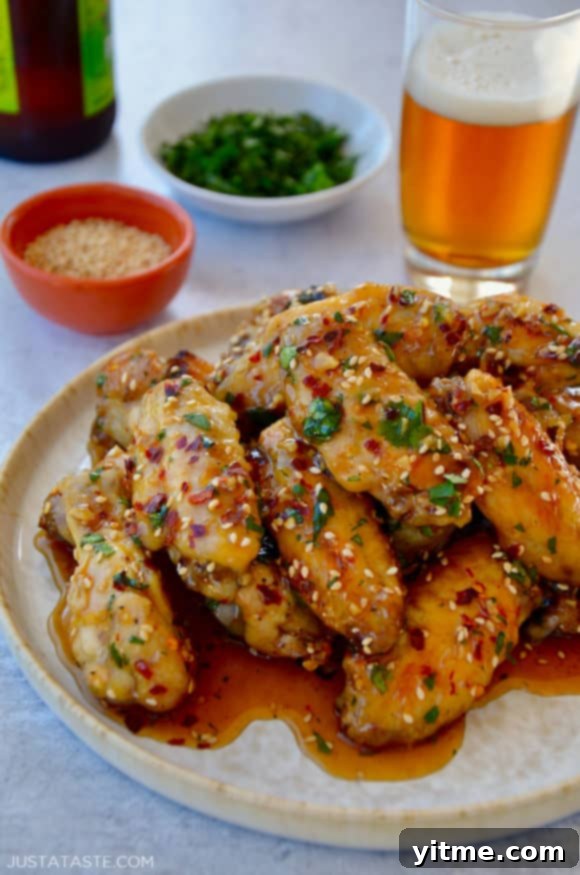 A white plate containing chicken wings with sesame seeds, cilantro and a beer in the background