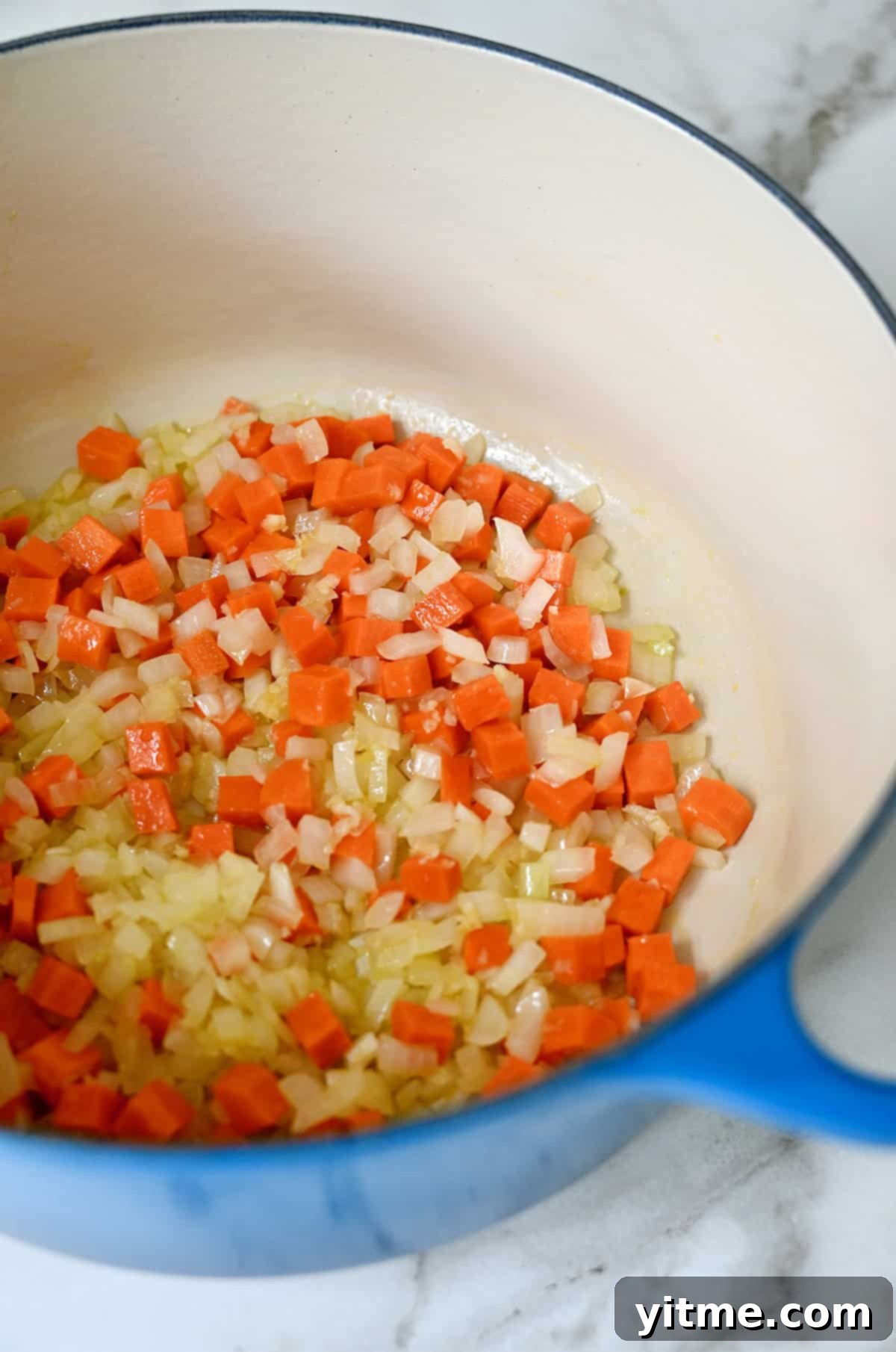 Sautéed diced carrots and onions in a blue Dutch oven.