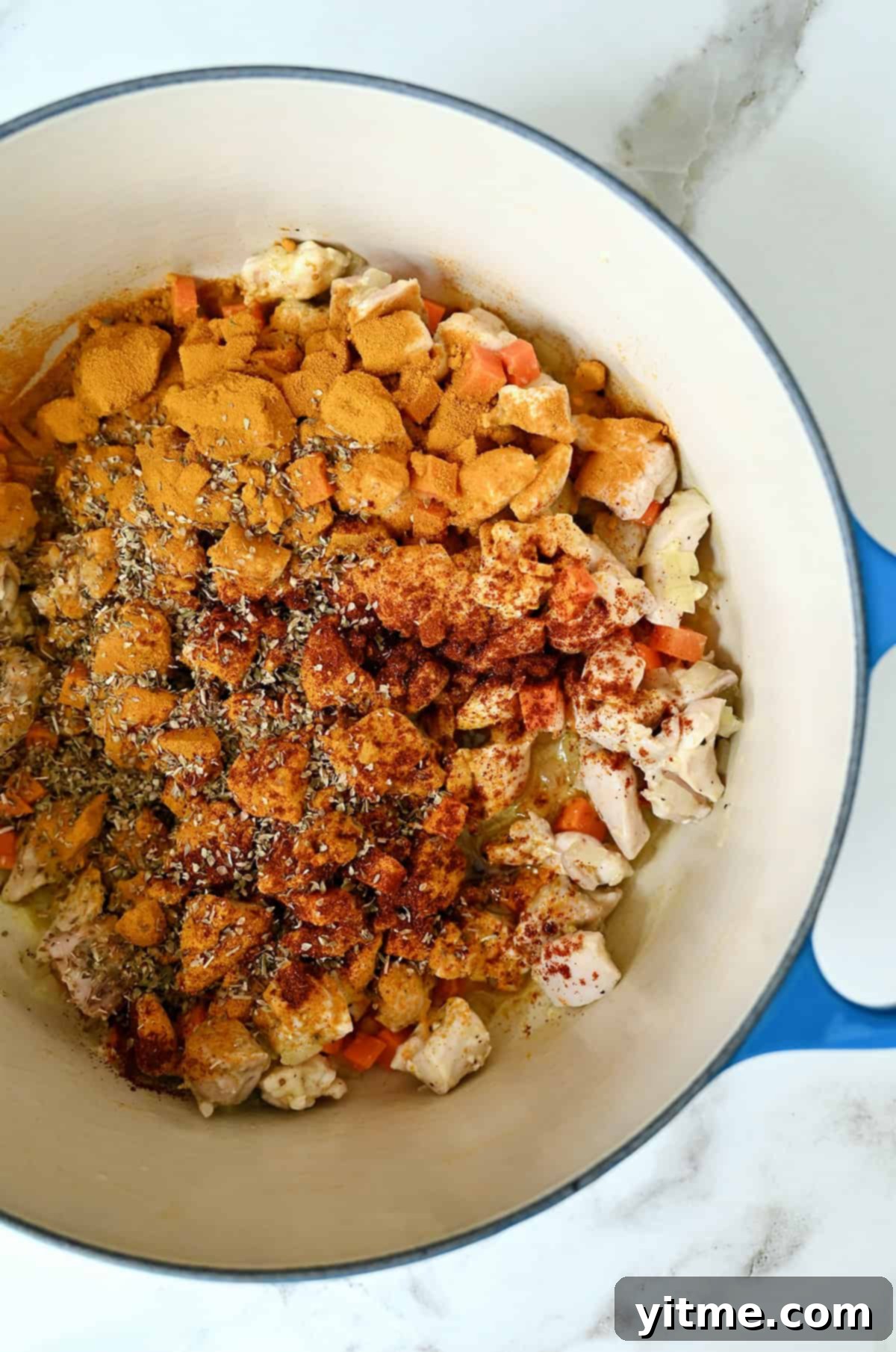 Turmeric, paprika and dried oregano atop cooked chicken thigh pieces and veggies in a Dutch oven.