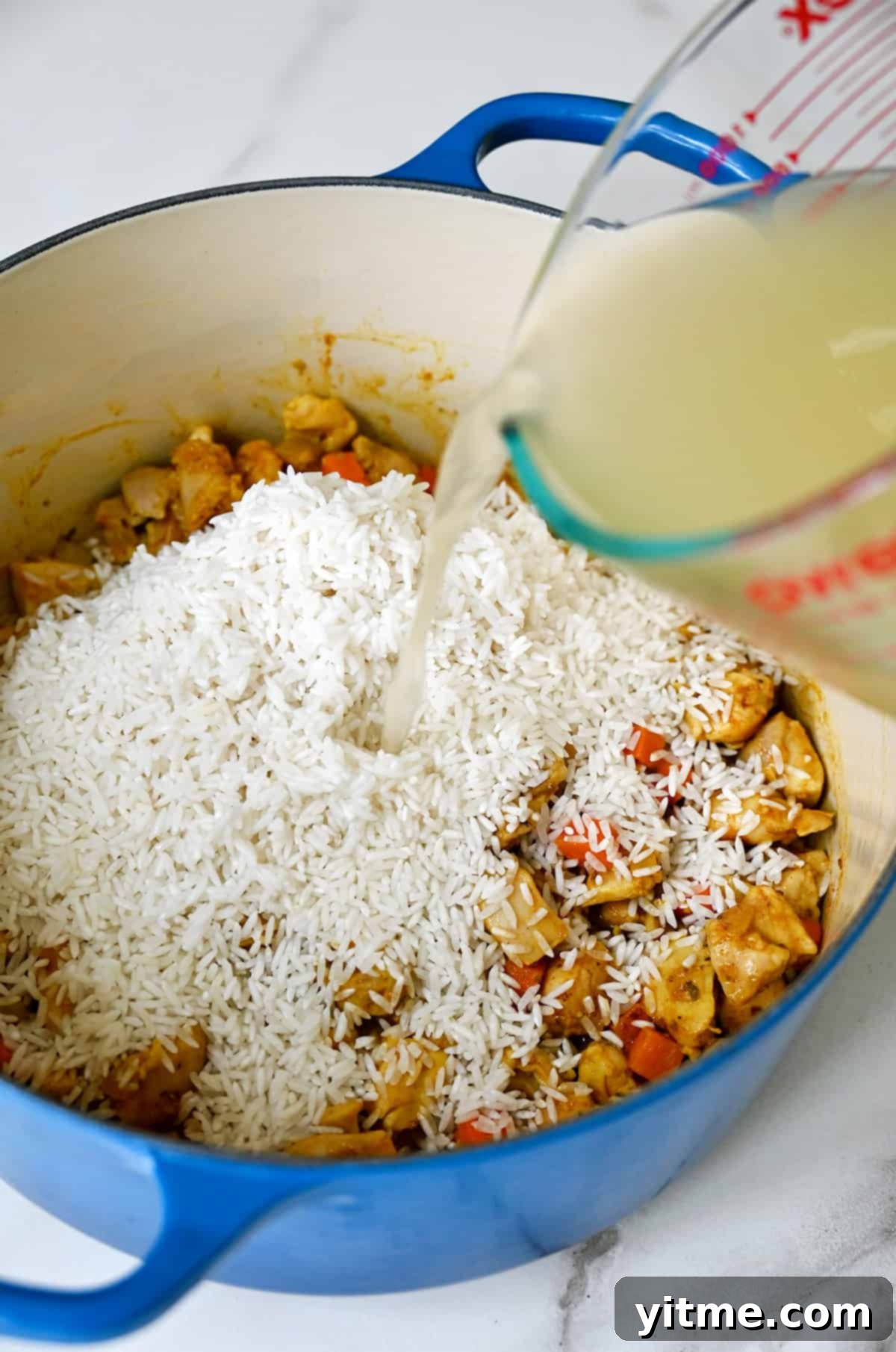 Chicken stock being poured over long-grain white rice in a Dutch oven.