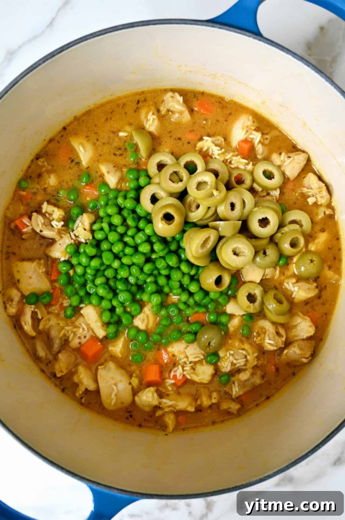 Sliced green olives and frozen peas with cooked chicken thighs and chicken stock in a Dutch oven.