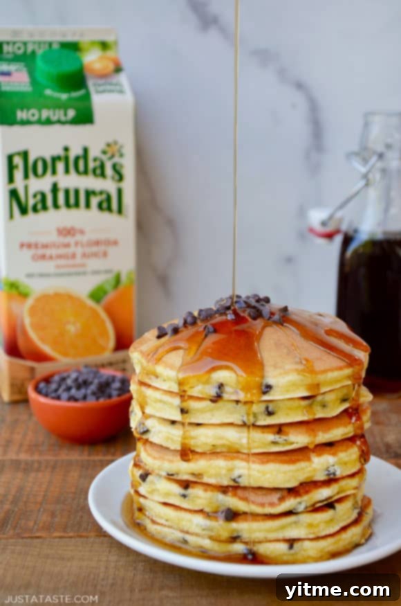 Stack of pancakes on a white plate with a carton of orange juice behind it