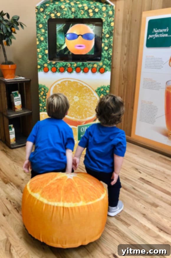 Two toddler boys sitting on an orange pillow watching a TV screen