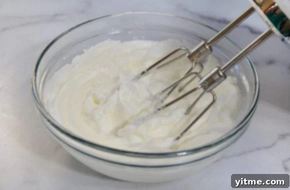 Egg whites being whipped with a handheld beater in a glass bowl