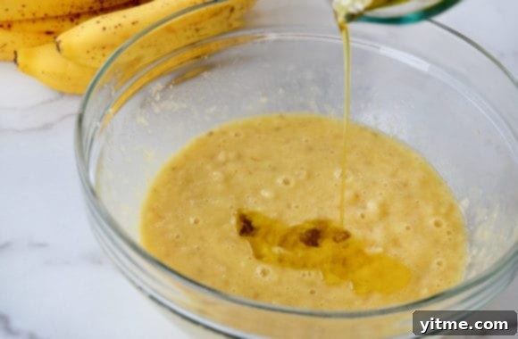 Olive oil being poured atop mashed bananas in glass bowl