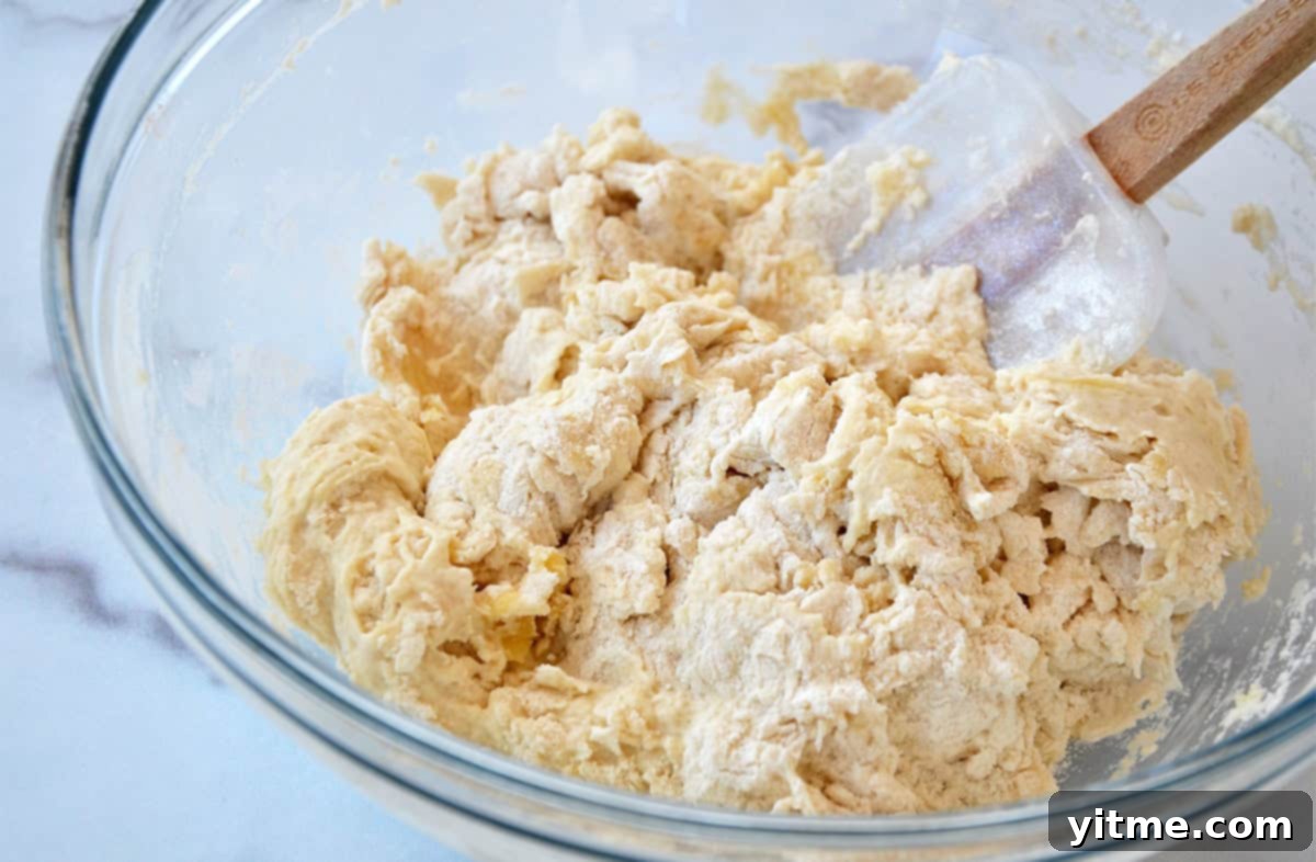A glass bowl containing pizza dough being stirred with a spatula, showing the ingredients coming together.