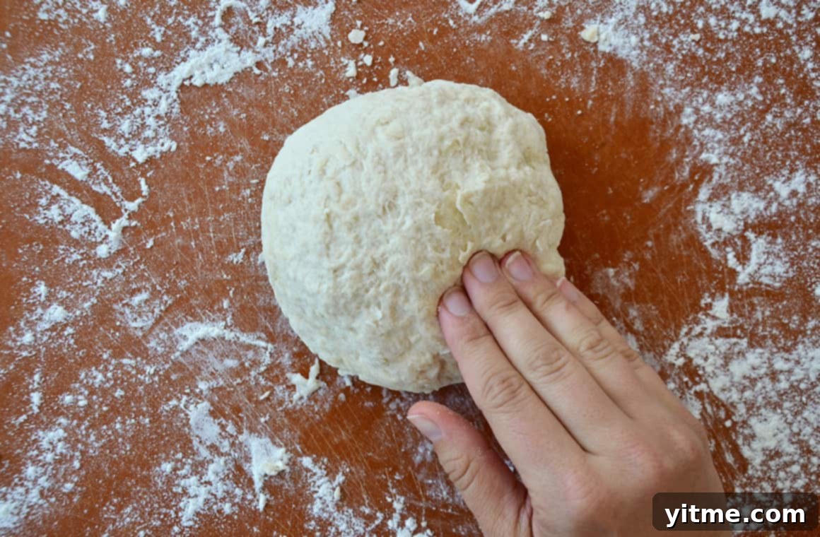 A wood cutting board lightly sprinkled with flour, with a perfectly smooth ball of pizza dough resting on top.