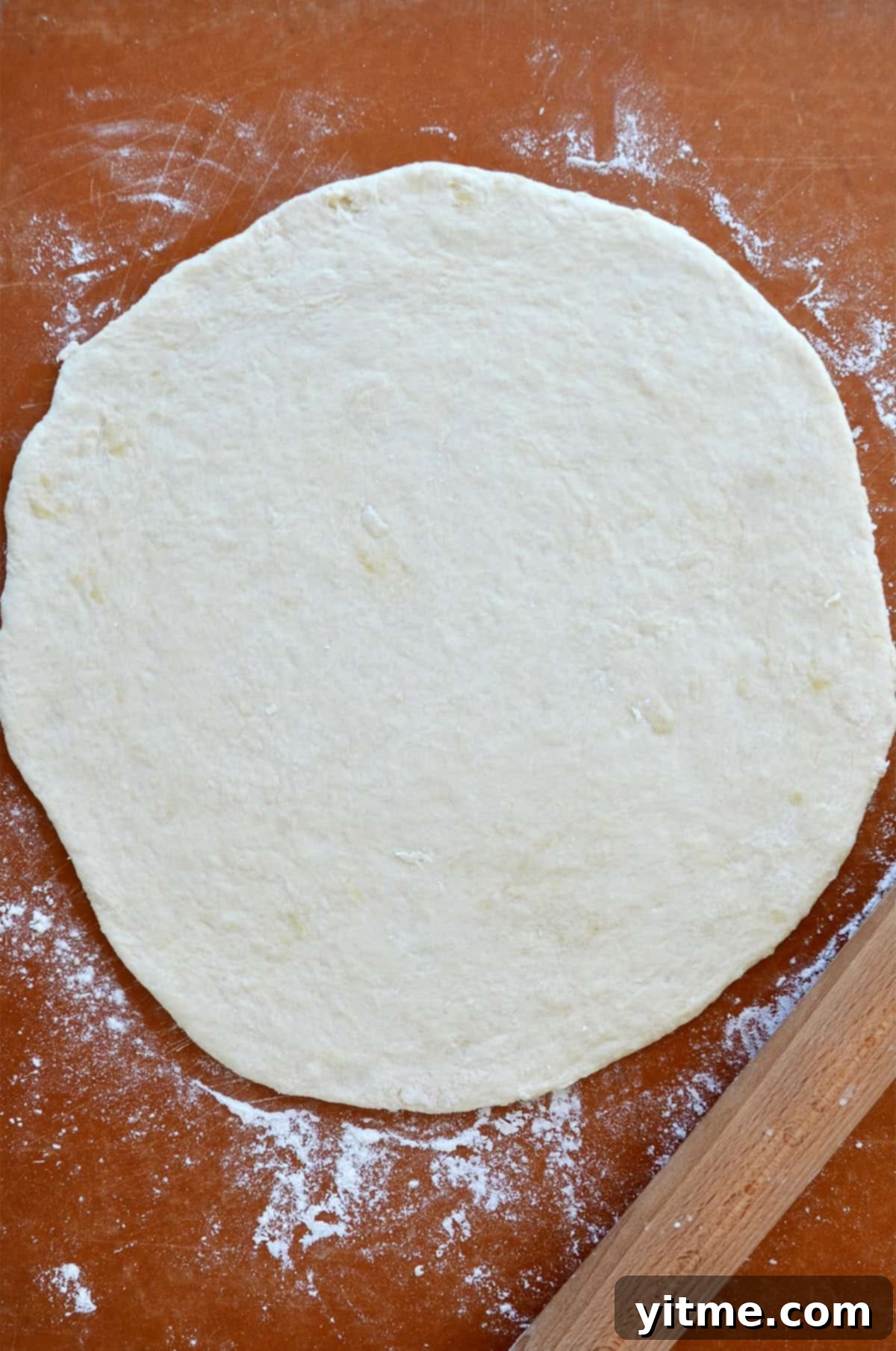 Rolled out no yeast pizza dough on a lightly floured surface, ready for toppings, positioned next to a rolling pin.