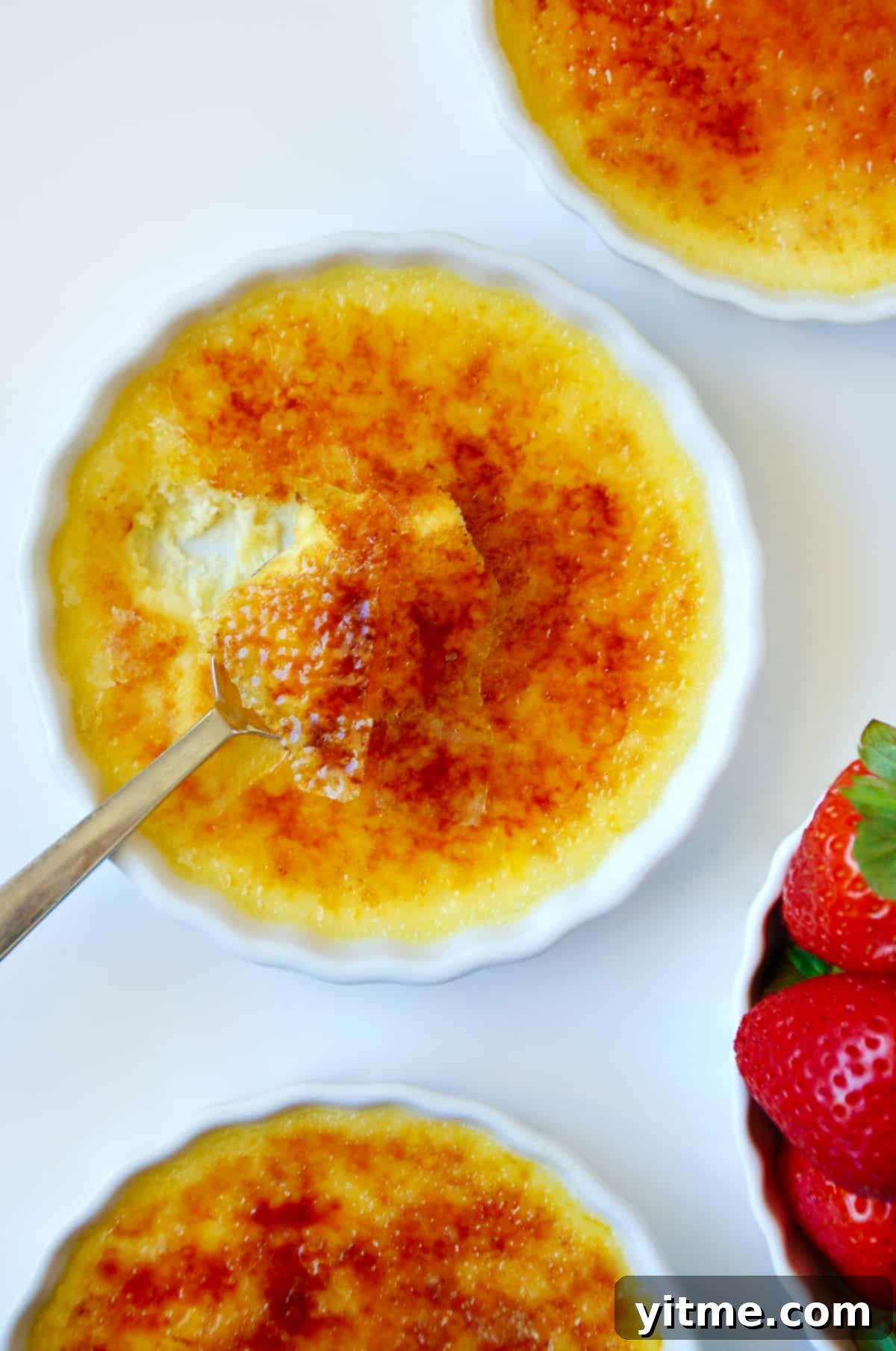 A crème brûlée cheesecake in a white tart dish next to a bowl of strawberries.