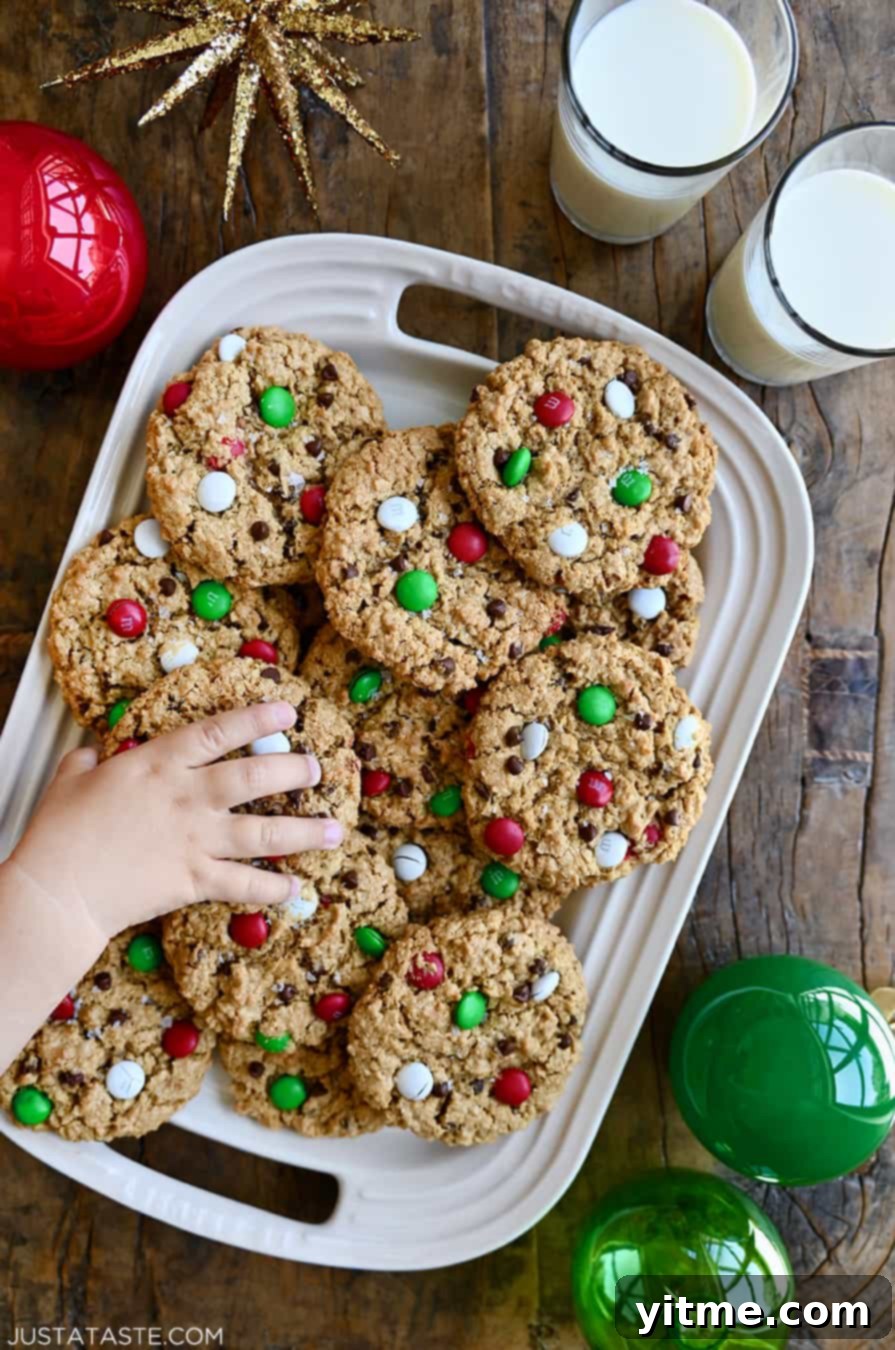 A child's hand reaches for a chewy holiday monster cookie on a platter full of cookies