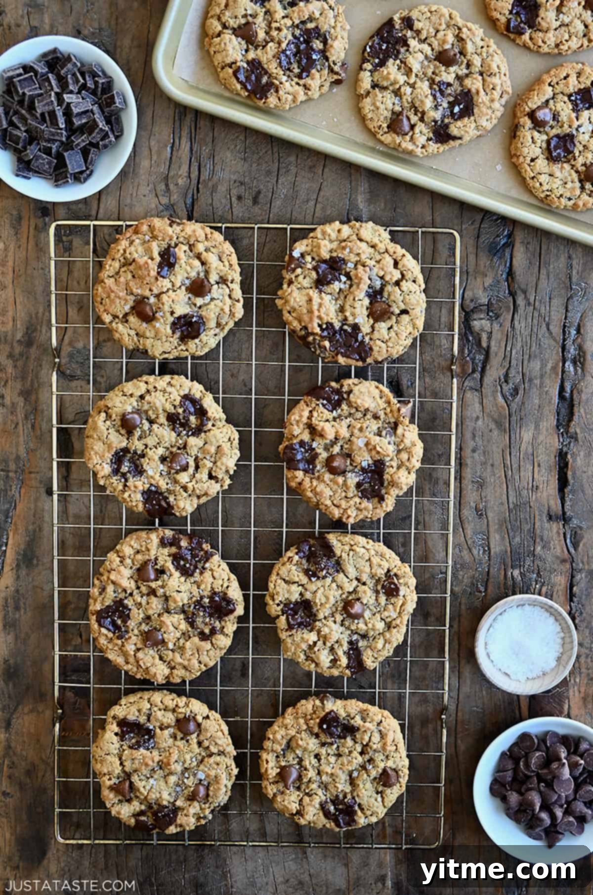 Flourless oatmeal cookies studded with chocolate chips and chunks on a wire cooling rack next to a small bowl containing large-flake sea salt.