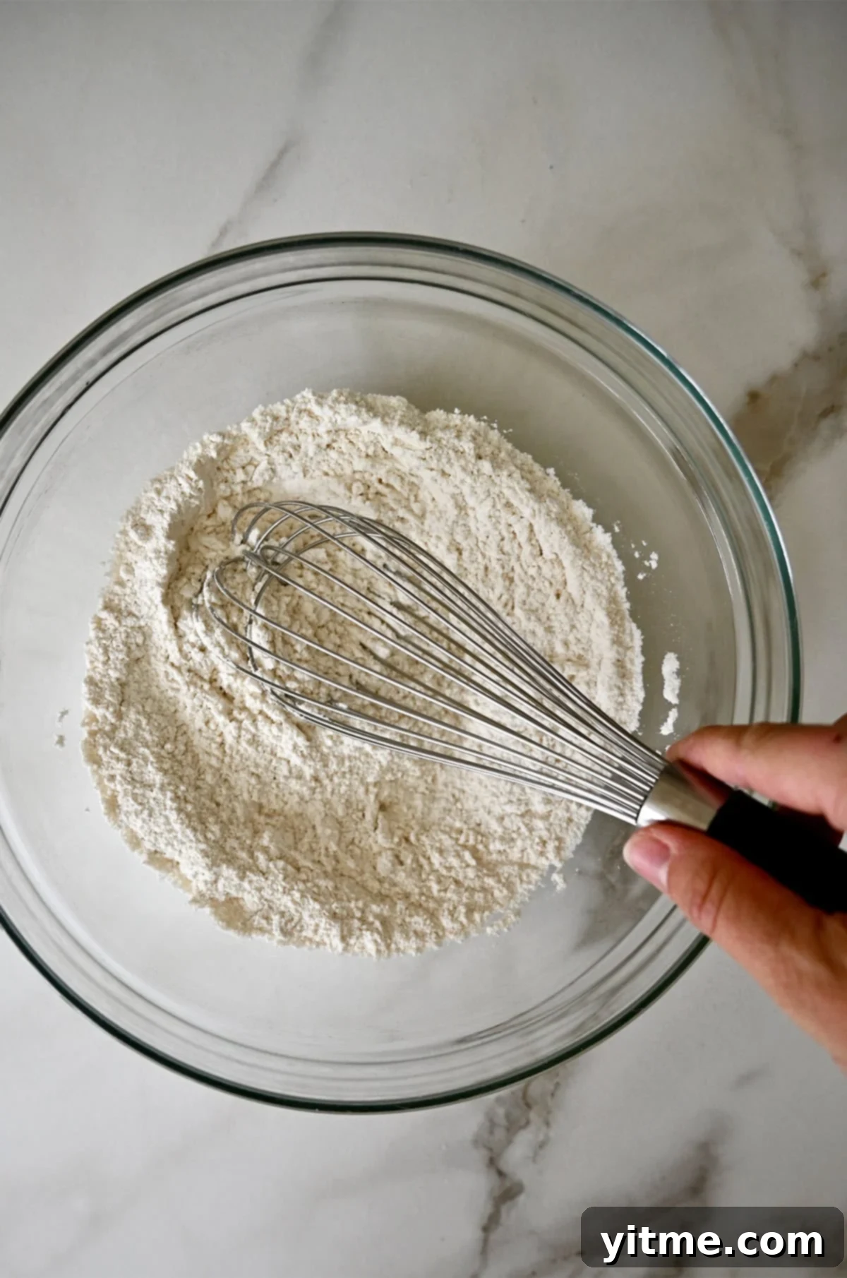 Mixing flour and baking powder in a bowl with a whisk.