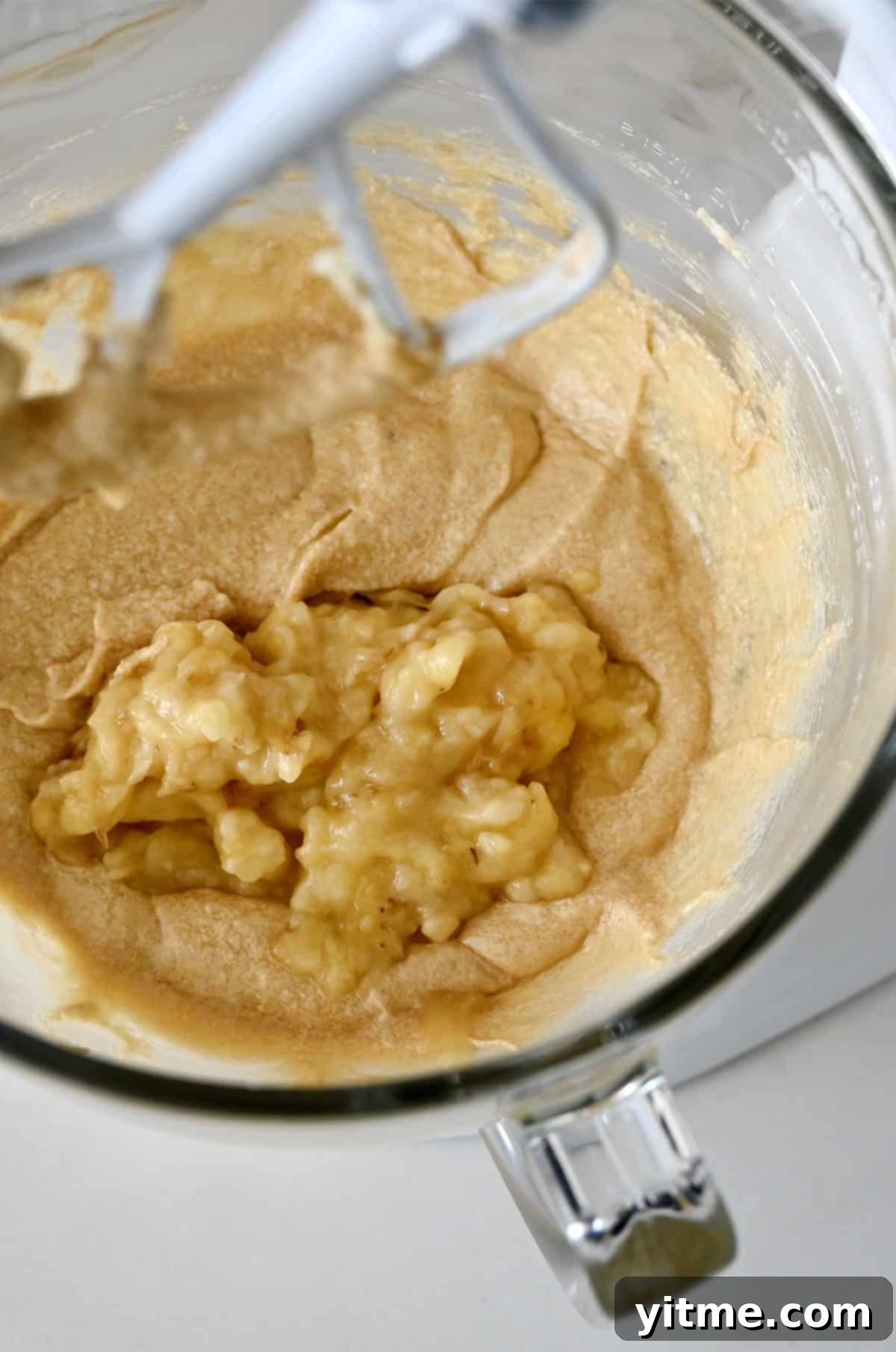 Adding mashed banana to a bowl with creamed butter, sugar, and vanilla.