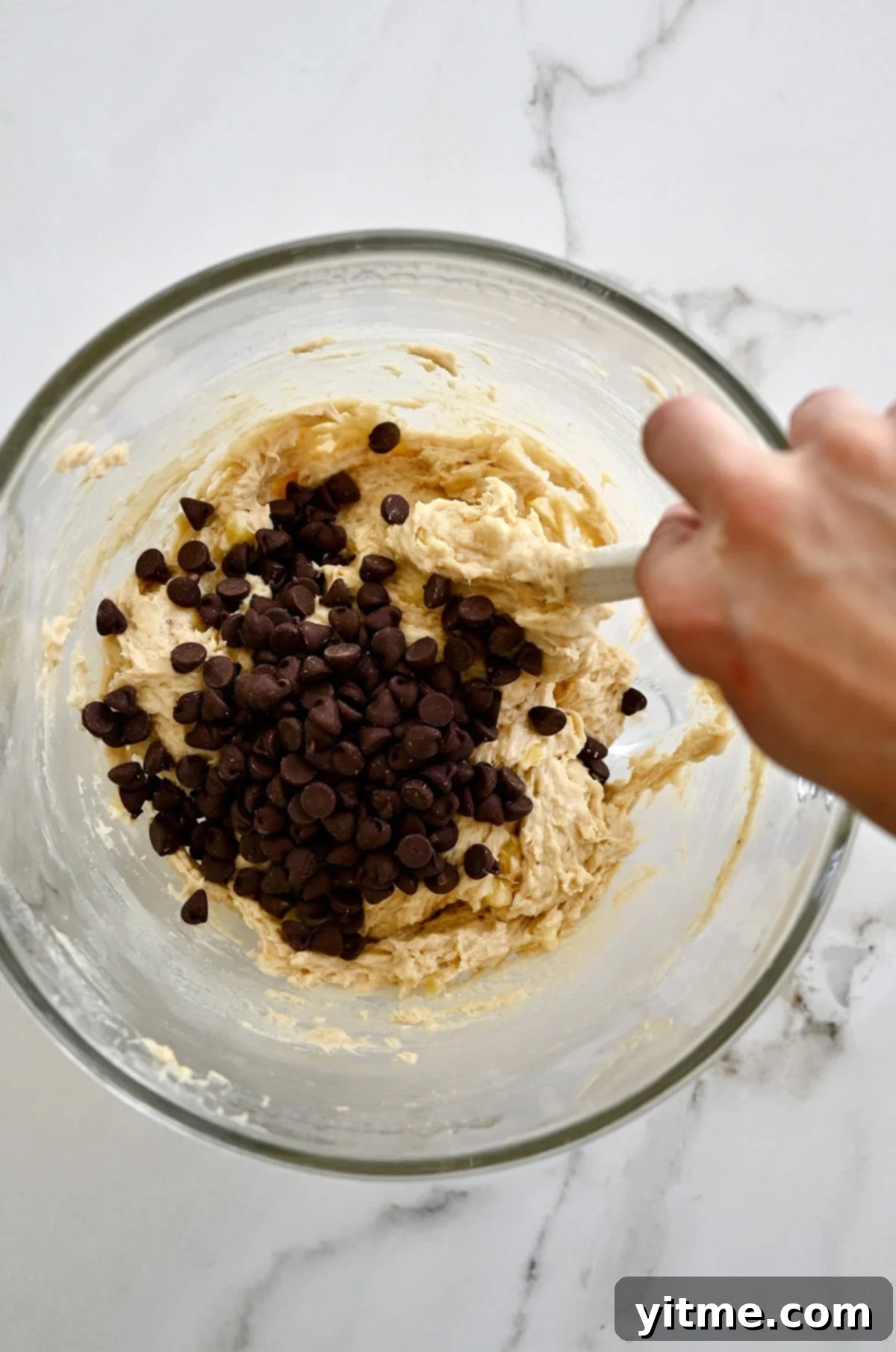 Stirring chocolate chips into banana cookie dough with a spatula.