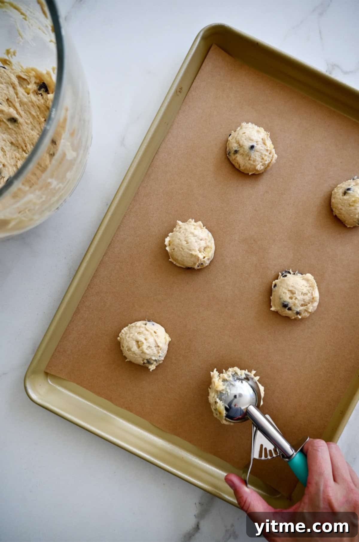 Scooping banana chocolate chip cookie dough onto a baking sheet.