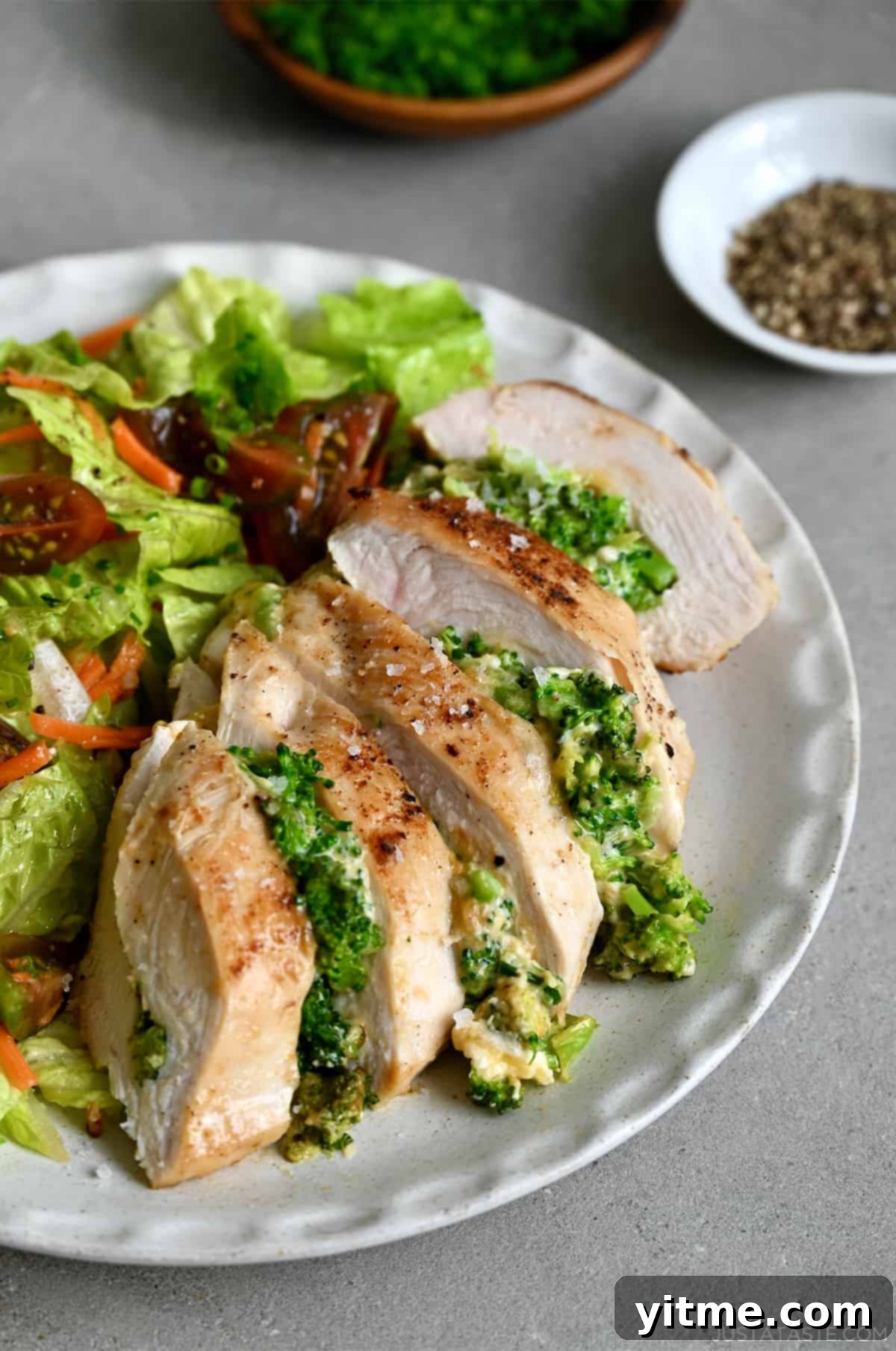 Broccoli cheddar stuffed chicken breast served on a dinner plate with a fresh green salad.