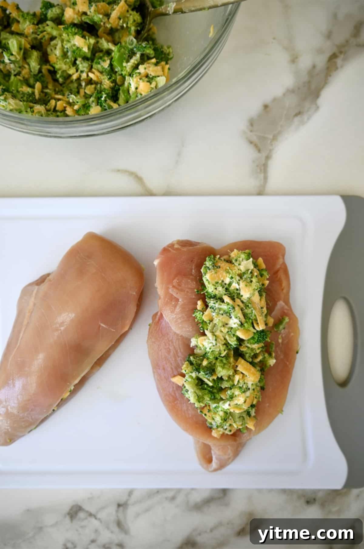 Broccoli and cheese filling stuffed into a raw chicken breast on a cutting board.