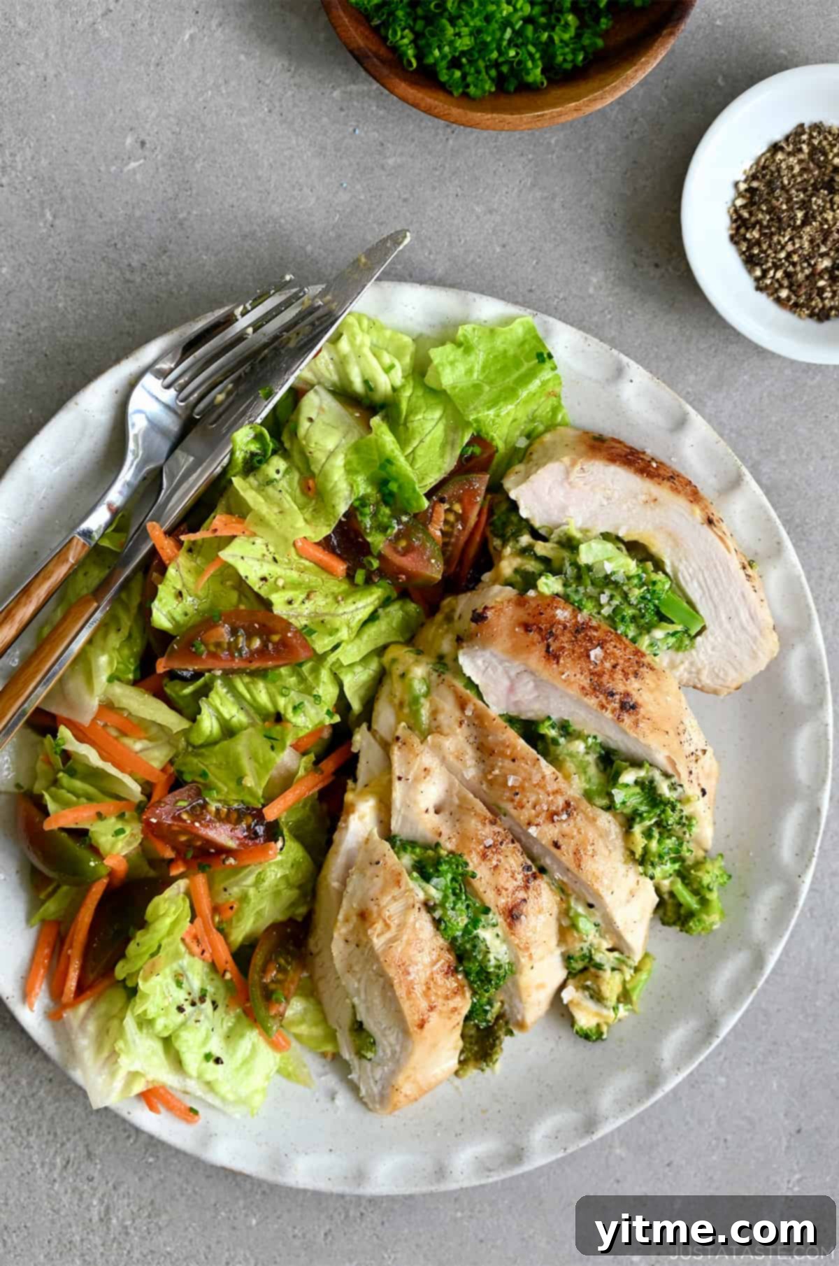 Broccoli and cheese stuffed chicken breast on a plate with romaine lettuce salad, and a fork and knife.