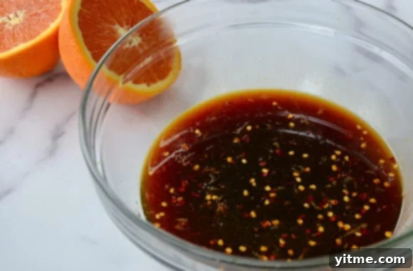 A clear bowl filled with flavorful stir-fry sauce, positioned next to a freshly sliced orange