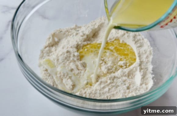 Pouring milk into a clear bowl containing flour and olive oil