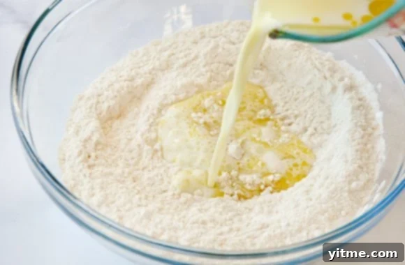 Milk and olive oil being poured from measuring cup into bowl containing flour 
