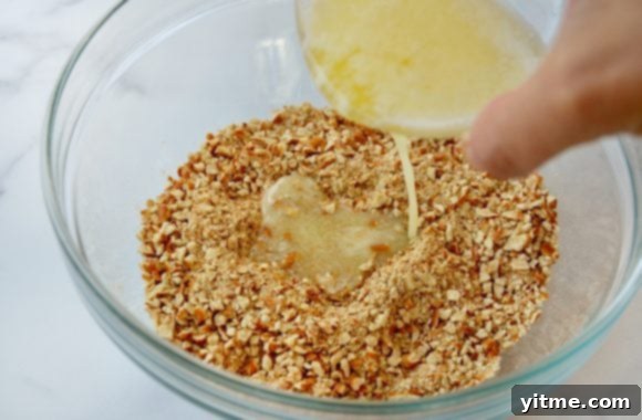Melting butter over crushed pretzels in a clear glass bowl for the pretzel crust