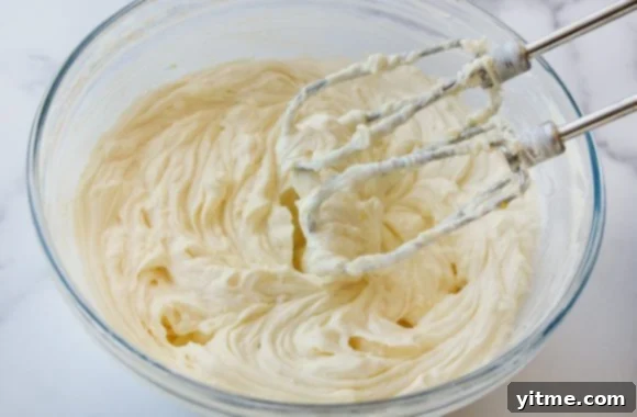 Using a handheld beater to mix the creamy cheesecake filling ingredients in a glass bowl
