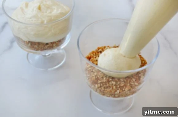 Piping cheesecake filling over the crushed pretzel base in individual dessert cups