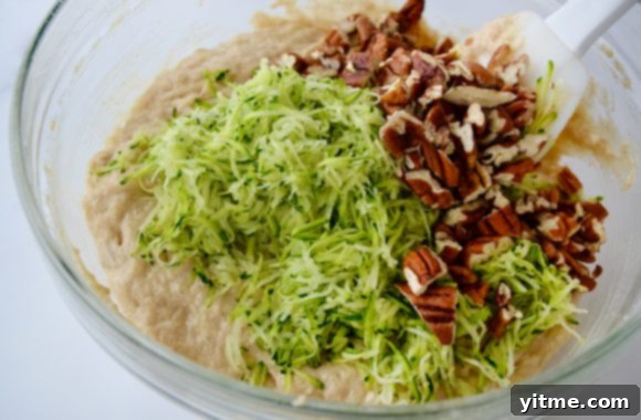 Glass bowl containing shredded zucchini, chopped pecans and muffin batter