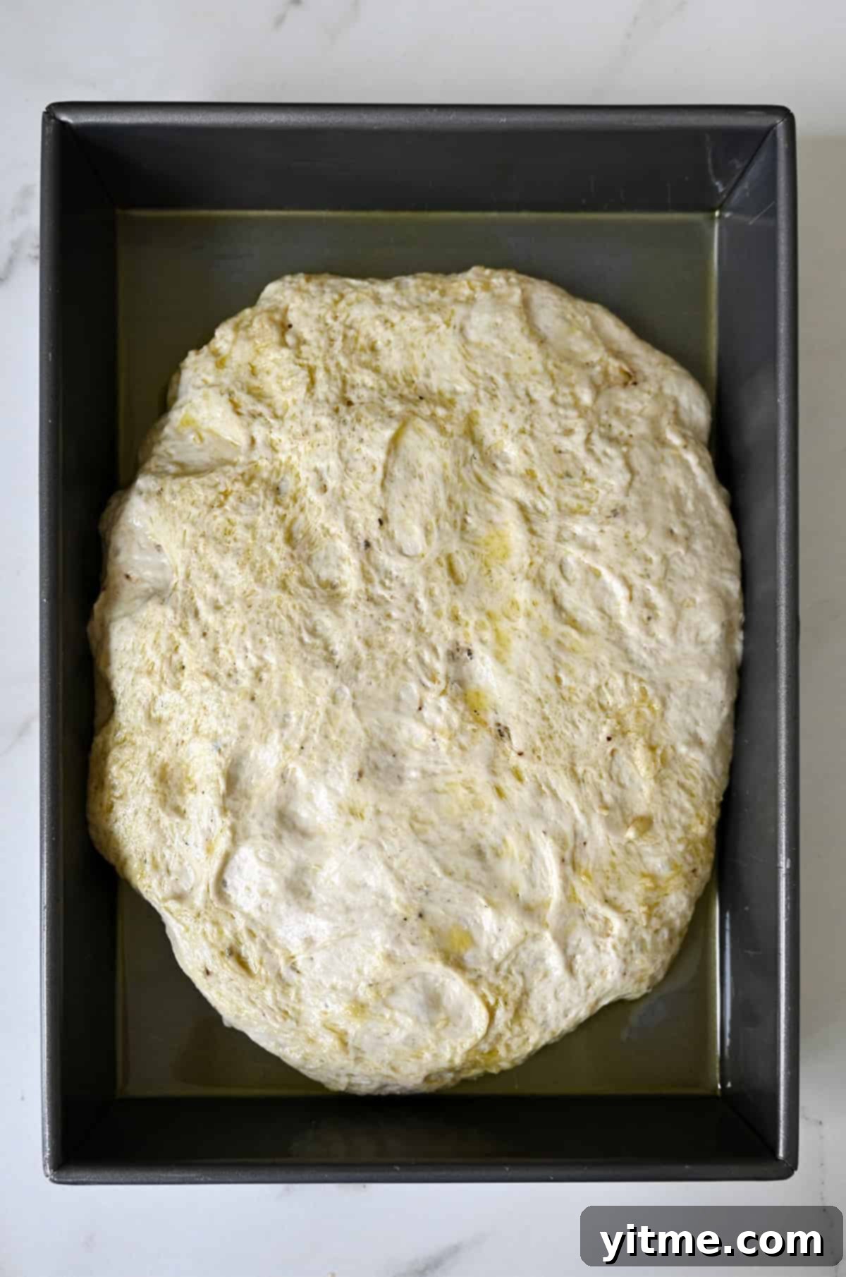 Focaccia dough in a 13x9 metal pan for the second rise.