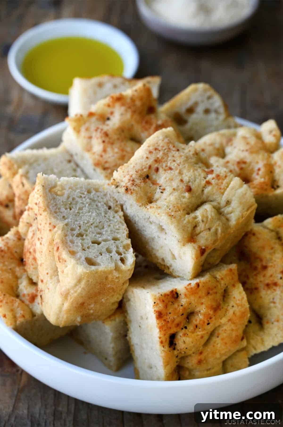 Slices of thick, Parmesan black pepper focaccia bread on a white serving plate.