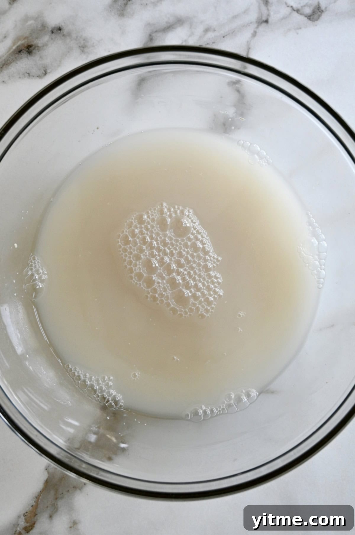 A large glass bowl containing a water and yeast mixture.