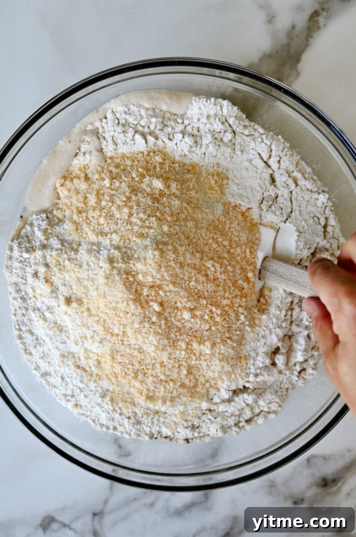 Dry ingredients being incorporated with a water and yeast mixture in a large bowl.
