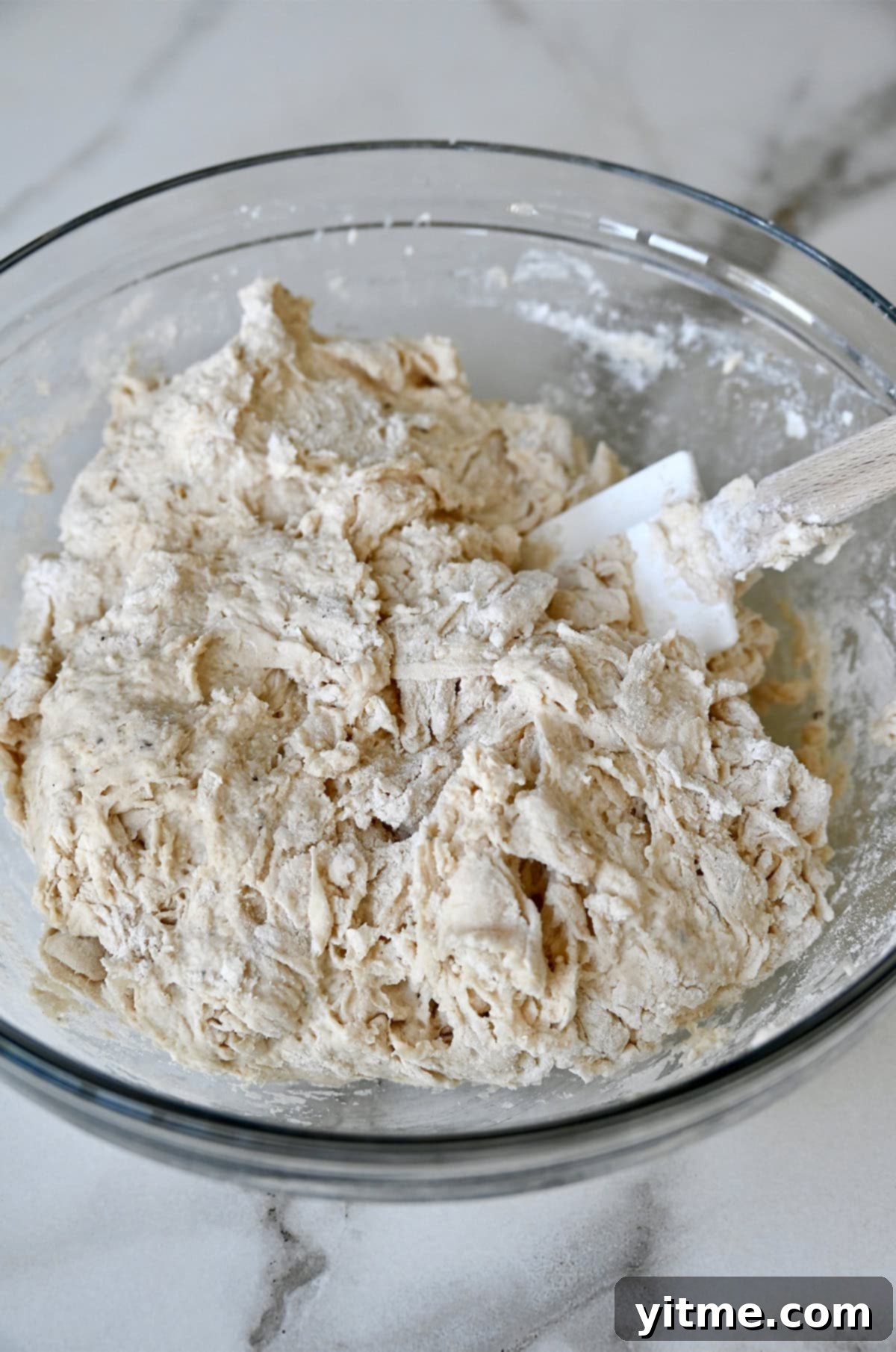 Shaggy focaccia dough in a large glass bowl with a rubber spatula.