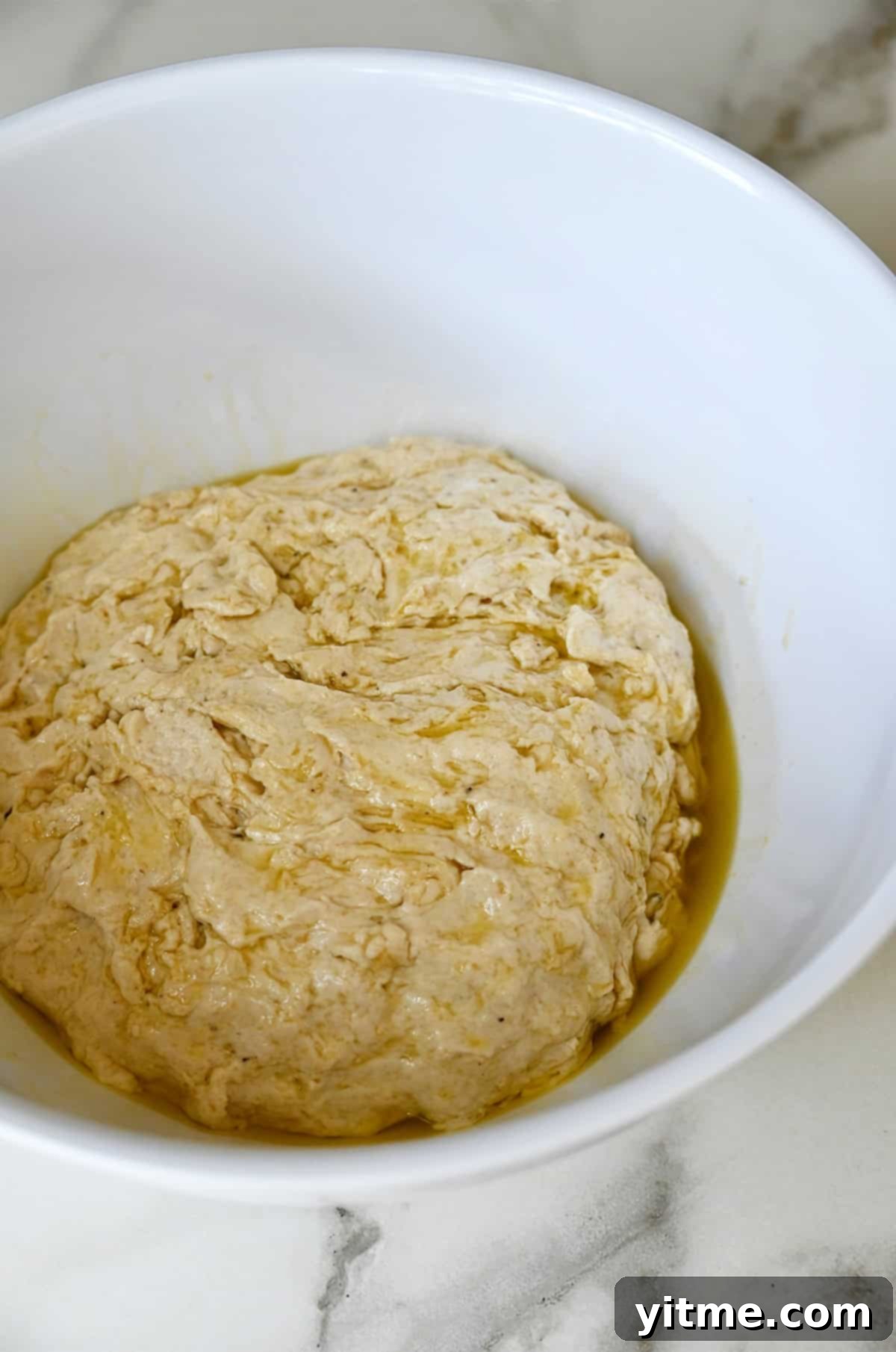 Dough coated in olive oil in a large white bowl.